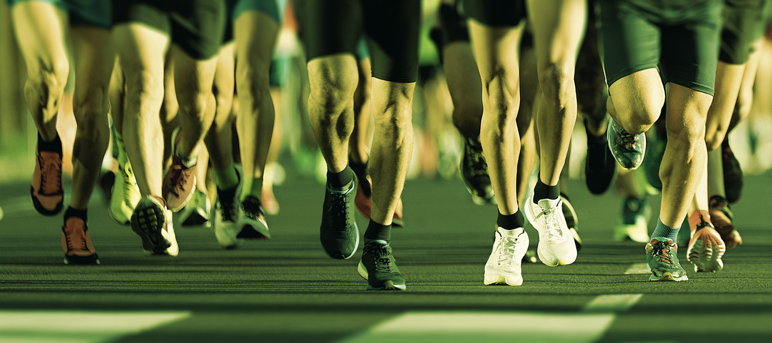 A number of people wearing different running shoe brands running on a road with a green tint.